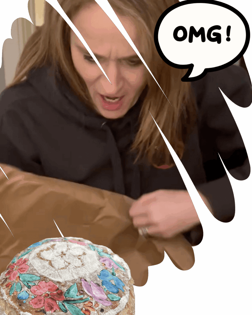 Jess OMG Woman gasping with surprise and delight while unboxing a painted loaf of bread decorated with colorful flowers.