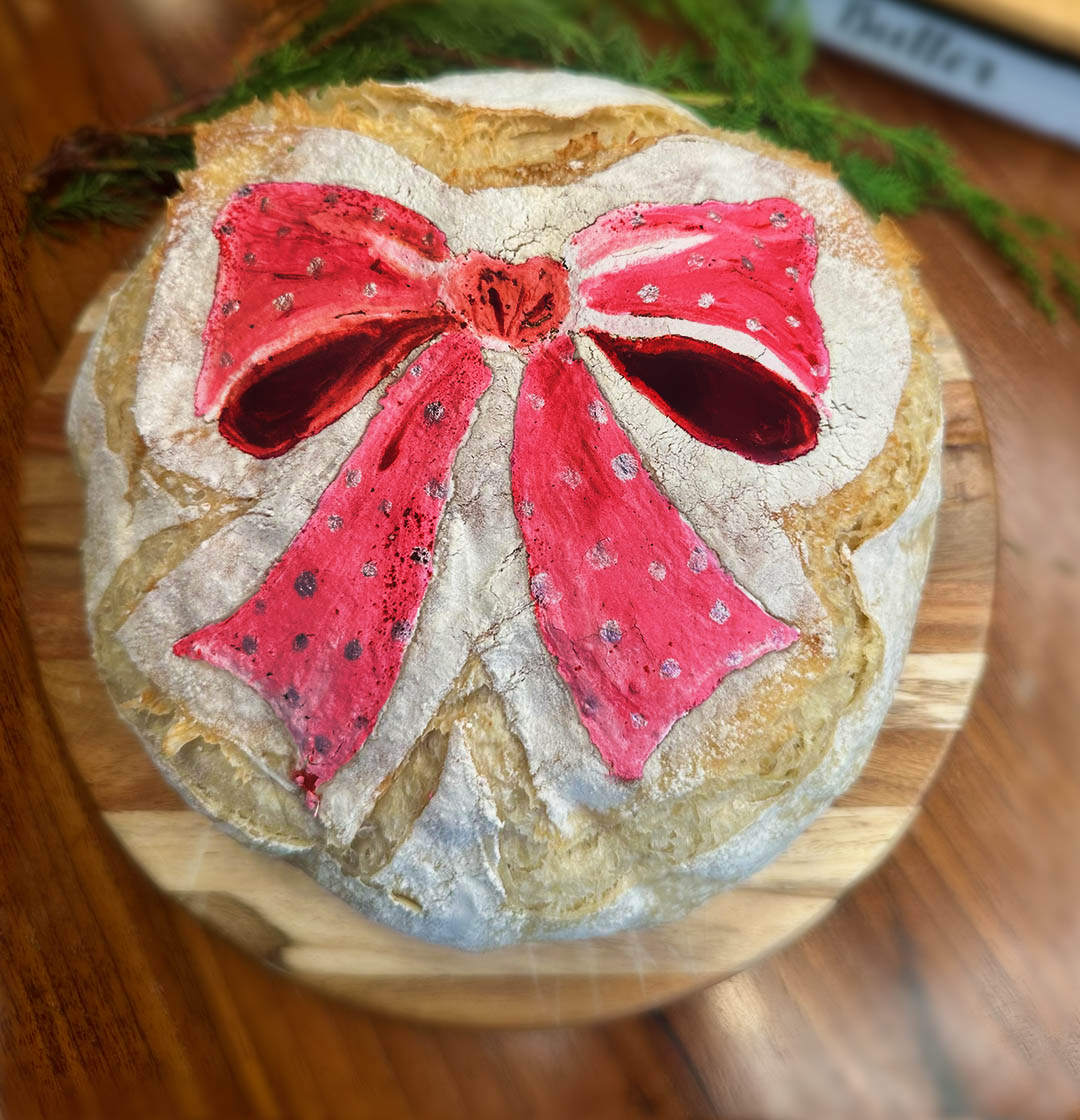 Image of attractive, smiling woman holding up delicious homemade bread, gorgeously and colorfully painted as a lion. Caption reads "This is bread!"